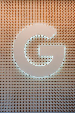 Large, stylized letter G backlit on textured wall with cylindrical protrusions, creating a 3D effect. Warm lighting, sleek design. Warm color palette. clipart