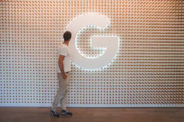 Person observes large illuminated letter G on wall with unique circular pattern in interior space. Setting implies corporate, educational, or exhibition environment. clipart
