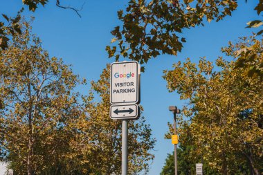 Google logolu park yeri, VISITOR Park tabelası, ve mavi gökyüzüne karşı ok ve sonbahar renkli ağaçlar. Google tesis alanına doğrudan ziyaretçiler.