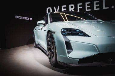 Lüks, mavi bir Porsche spor arabası lüks bir etkinlikte sergileniyor. Gösterişli tasarım, amblem ve alaşım tekerlekleri sergileniyor. Dramatik ışıklandırma onun özelliklerini vurgular.
