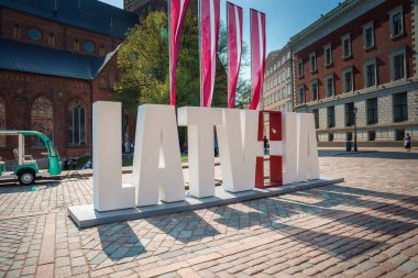 Riga, Letonya 'da güneşli bir gün. Önünde LATVIA harfleri, bayrak renkleri. Tramvay otobüsü, tarihi bina, temiz gökyüzü. AB 'de 20 yılı kutluyoruz.