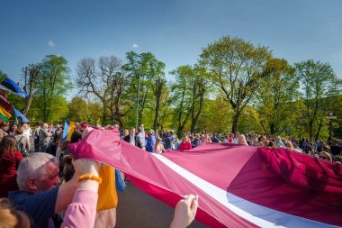 Vibrant celebration in Riga, Latvia with people carrying flags Latvian flag prominently featured. Joyful atmosphere near the Freedom Monument. EU membership celebration. clipart
