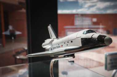 Close up of Space Shuttle Endeavour model with US flag and NASA logo, on display. Background shows indoor setting with reflection and window view. Possibly in Arizona. clipart