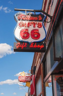Canlı kırmızı ve beyaz neon işareti, Hediyelik Eşyalar 66 Hediye Dükkanı, mavi gökyüzüne karşı. Coca Cola logosu klasik bir dokunuş katıyor. Williams Town yakınlarında, Büyük Kanyon.