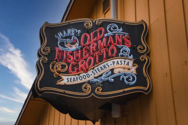 Old Fishermans Grotto için klasik restoran tabelası. Siyah arkaplanda süslü kırmızı ve beyaz harfler var. Deniz ürünleri, biftek ve makarna servis edilir. Kıyı bölgesinde yer almaktadır..