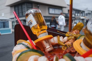 Şiş karides, sebze ve sos ile renkli yemek tabağı, bir şişe bal renkli alkol, ve arka planda geleneksel bina ile açık hava seti.