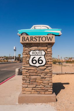 ABD 'nin 66. Otoyol' daki Barstow 'u aydınlatan bir anıtı keşfedin. Taş taban, BARSTOW ve ROUTE 66 metin, klasik araba, açık gökyüzü, çöl zemin.