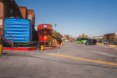 Sunny day scene in Barstow, USA with old Route 66 vibes. Wooden buildings, parking lot, and colorful train car add charm to this quiet, historic area. clipart