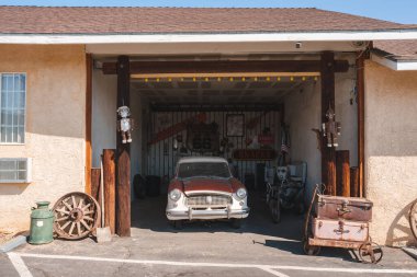 Vintage workshop with antique car on Route 66 in Barstow, USA. Rustic garage exterior, nostalgic decor, and sunny skies create a tranquil Americana scene. clipart