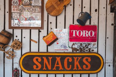 Vintage Americana decor featuring a SNACKS sign on Route 66 in Barstow, USA. Memorable items include Route 66 memorabilia, a cowboy hat, TORO dealer sign, and fishing plaque. Rustic charm abounds clipart