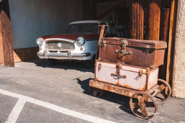 Vintage scene in Barstow, USA along Route 66. Rusted luggage cart with leather suitcases, classic car from 1950s 60s, sunny day evoking Americana nostalgia. clipart