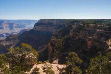 Açık mavi gökyüzünün altındaki Büyük Kanyon 'un nefes kesici panoramik manzarasını keşfedin. Arizona, ABD 'de geniş jeolojik manzaralar kırmızı ve kahverengi kaya oluşumlarını sergiliyor..