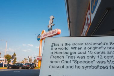 Oldest McDonalds restaurant in the world with iconic neon Chef Speedee mascot sign and golden arches. Possibly in Los Angeles area. Clear blue sky. clipart