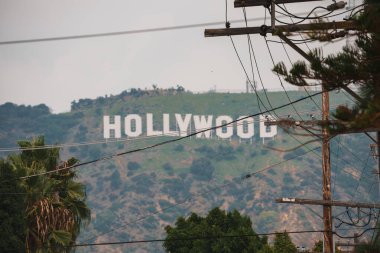 Devrilen tepelere karşı uzaktan görülen ikonik Hollywood tabelası, kısmen elektrik hatlarıyla gizlenmiş. Los Angeles, Kaliforniya 'da şehir merkezi. Sisli atmosfer.