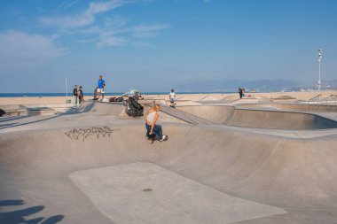 Venice Beach Kaykay Parkı, Los Angeles 'ta kaykay yapan genç bir kadın. Yumuşak beton kıvrımlar, rampalar ve seyirciler. Sahilde güneşli bir gün. Canlı bir buz pateni kültürü havası var..