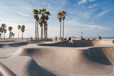 Los Angeles, Kaliforniya 'daki Venice Beach Paten Parkı' nın canlı enerjisini deneyin. Güneşli bir sahneye dalın patenciler ve plaja gidenlerle çarpıcı mavi bir arka plana.