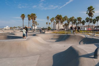 Los Angeles 'taki Venice Beach Paten Parkı' nda güneşli bir gün. Patenciler hareketli parkta beton kase, kıvrımlar ve rampalarla dans ediyorlar. Palmiye ağaçları, SoCal havası, plajdaki sıradan atmosfer..
