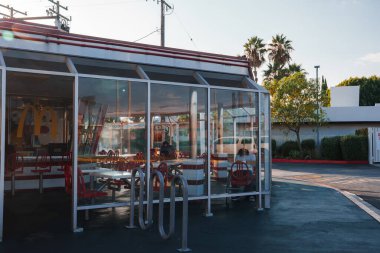 Outdoor diner seating area with retro design and warm sunset glow. Classic diner chairs, clear skies, and bike racks. Possibly in Los Angeles, tranquil and nostalgic ambiance. clipart