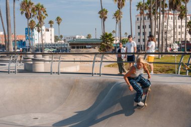 Venice Beach Paten Pisti, Los Angeles 'ta kaykaycı. Yumuşak kıvrımlar, palmiye ağaçları, izleyiciler ve güneşli gökyüzü canlı bir Güney Kaliforniya havası yaratır..