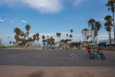 Explore an outdoor basketball court under clear skies with a leisurely vibe in Venice Beach, Los Angeles. Palm trees and open space create a calm, inviting atmosphere. clipart