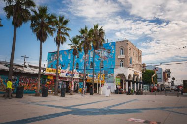 Venice Beach, Los Angeles 'ta canlı bir şehir manzarası, palmiye ağaçları, sokak sanatı, insanlar ve dükkanlar. Ziyaretçilerin ve yerlilerin ilgisini çeken canlı, çeşitli mahalleler..