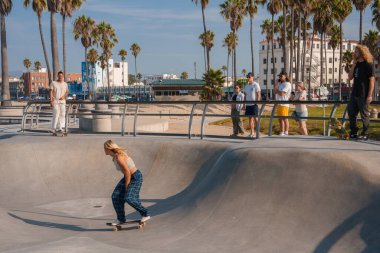 Venice Beach, Los Angeles 'ta kaykay sahnesi. Güneşli bir gökyüzünün altında kaykaycılar, izleyiciler ve palmiye ağaçları var. Açık hava aktiviteleri için mükemmel..
