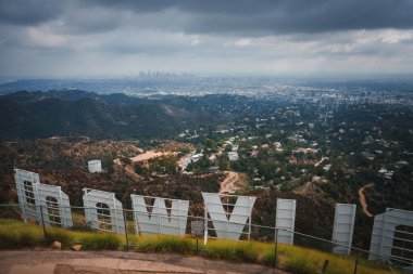 Los Angeles 'a bakan gökyüzü bulutlu ikonik Hollywood tabelası. Dağlardan yakalanmış, genişleyen şehir manzarasını ve şehir merkezindeki ufuk çizgisini gösteriyor..