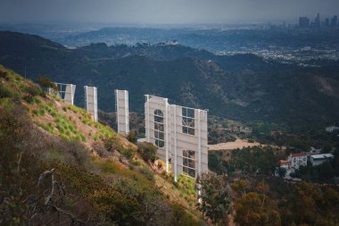 Iconic Hollywood Sign viewed from behind against hills and cityscape of Los Angeles at dawn or dusk. Unique perspective showcasing structural supports and surroundings. clipart