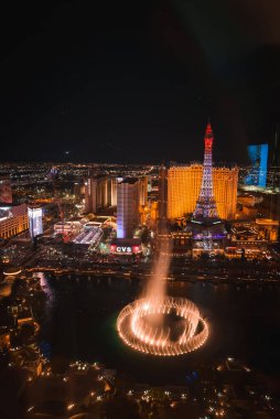 Aerial night view of vibrant Las Vegas Strip with Bellagio fountains, Eiffel Tower replica, and bright city lights creating dynamic, electric atmosphere. clipart
