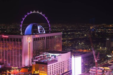 Vibrant night view of Las Vegas Strip featuring High Roller Ferris wheel in purple lighting, Flamingo Las Vegas Hotel, city lights extending into horizon. clipart