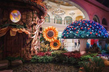 Las Vegas Strip Oteli 'nde renkli çiçek mantarları ve yemyeşil bahçeli canlı bir ev sahnesi. Şatafatlı dekorlar ve hayat dolu ziyaretçiler büyüleyici bir ortam yaratıyor..