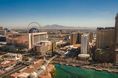 Daytime aerial view of the vibrant Las Vegas Strip, showcasing luxurious resorts, hotels, casinos, and the iconic High Roller Ferris wheel under a clear blue sky. clipart