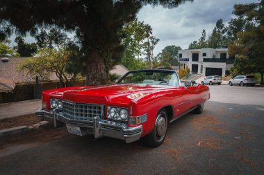 Vintage red convertible car from possibly the 1970s, resembling a Cadillac, parked on a residential street in Los Angeles. Serene, nostalgic ambiance. clipart