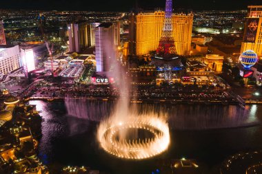 Vibrant aerial night view of Las Vegas Strip with Bellagio fountain show in full swing. Eiffel Tower replica shines in background among bustling city lights. clipart