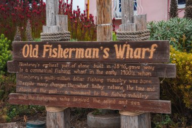 Monterey, California 'daki Old Fisherman Rıhtımı' nda ahşap tabela. Rıhtımın 1846 'dan günümüze olan tarihi. Renkli bitkiler ve bulutlu gökyüzü ile yıpranmış, kırsal görünüm.