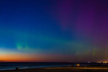 Riga ve Jurmala, Letonya 'daki bir plajda Aurora Borealis' in göz kamaştırıcı görüntüsü. Parlak yeşil, mavi ve mor renkler gece gökyüzünü aydınlatır. Karanlık ufukla çelişir..