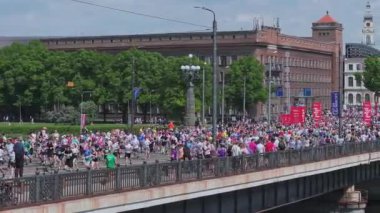 Riga Rimi Maratonu 2024. Maraton etkinliği sırasında şehirde koşan kalabalığın hava görüntüsü. Toprak setten başlayın ve insanlar Daugava nehrinden şehir merkezine doğru koşun..