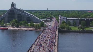 Riga Rimi Maratonu 2024. Maraton etkinliği sırasında şehirde koşan kalabalığın hava görüntüsü. Toprak setten başlayın ve insanlar Daugava nehrinden şehir merkezine doğru koşun..