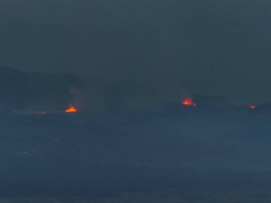 İzlanda 'da volkanik bir patlamanın havadan görünüşü uzaktaki parlak turuncu alevlerden oluşan karanlık ve puslu bir manzarayı gösteriyor..