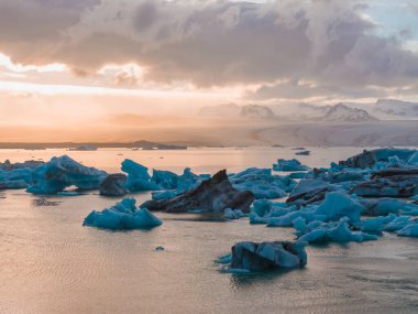 İzlanda 'daki Jokulsarlon buzulunda eriyen zümrüt turkuaz mavisi buzdağlarıyla güzel bir gün batımı..