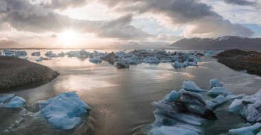 İzlanda 'daki Jokulsarlon buzulunda eriyen zümrüt turkuaz mavisi buzdağlarıyla güzel bir gün batımı..