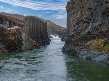 Sakin, derin mavi bir nehir, İzlanda 'nın engebeli dağlarına karşı uzanan karanlık volkanik kayalardan oluşan dar bir kanyon boyunca esiyor..