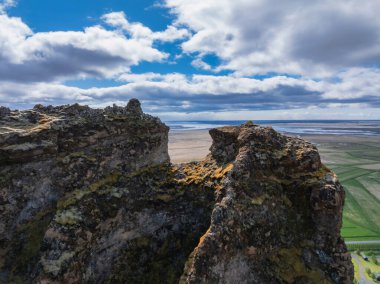 İzlanda 'da düz, yeşil bir manzarayı ortaya çıkaran iki kayalık uçurumun dramatik hava manzarası. Beyaz bulutlu mavi gökyüzü engebeli güzelliği arttırır..