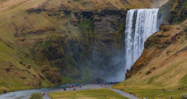 Gün batımında İzlanda 'nın etkileyici güzellikte doğası. Skogafoss şelalesi İzlanda 'nın ünlü bir doğal dönüm noktasıdır. Turistler ünlü şelale yakınlarında ata binerler..