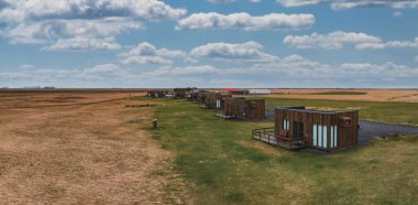 Benzer modern ahşap kulübelerin uçsuz bucaksız karalarla çevrili çimenli bir arazide, İzlanda 'da beyaz bulutlu mavi bir gökyüzünün altında çekilmiş görüntüleri..