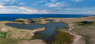 Stunning aerial view of Icelands coastline featuring deep blue lakes and ponds, surrounded by green grass and brown rock under a bright blue sky with white clouds. clipart