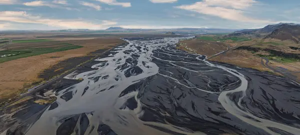 Stock image An aerial view of a meandering river with a dark gray bed and light gray water flow, surrounded by a brown, barren landscape in Iceland.