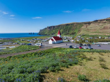 İzlanda 'daki Vik i Myrdal tepesindeki ikonik kırmızı çatılı kilisenin hava manzarası. Kilise dramatik siyah kumsala ve yemyeşil tepelere bakıyor..