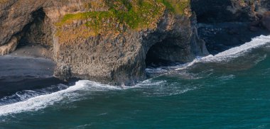 İzlanda 'da bazalt sütunlardan oluşan büyük bir mağaranın olduğu siyah kumlu bir sahilin göz kamaştırıcı hava manzarası. Dalgalar kıyıya çarpıyor, İzlanda volkanik tarihini gözler önüne seriyor..