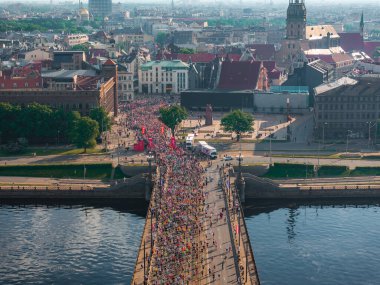 Riga Rimi Maratonu 2024 'ün enerjisini çeken hava çekimi. Koşucular Riga, Letonya 'da sarmal bir hat oluştururken, şehir binaları çarpıcı bir zemin oluşturuyor..